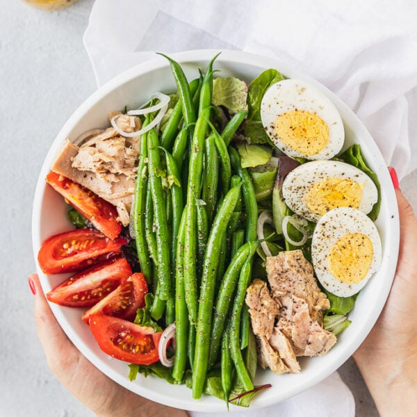 hands holding bowl of nicoise salad with hard boiled eggs