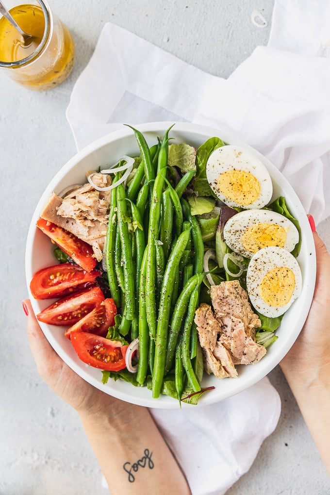 hands holding bowl of nicoise salad with hard boiled eggs