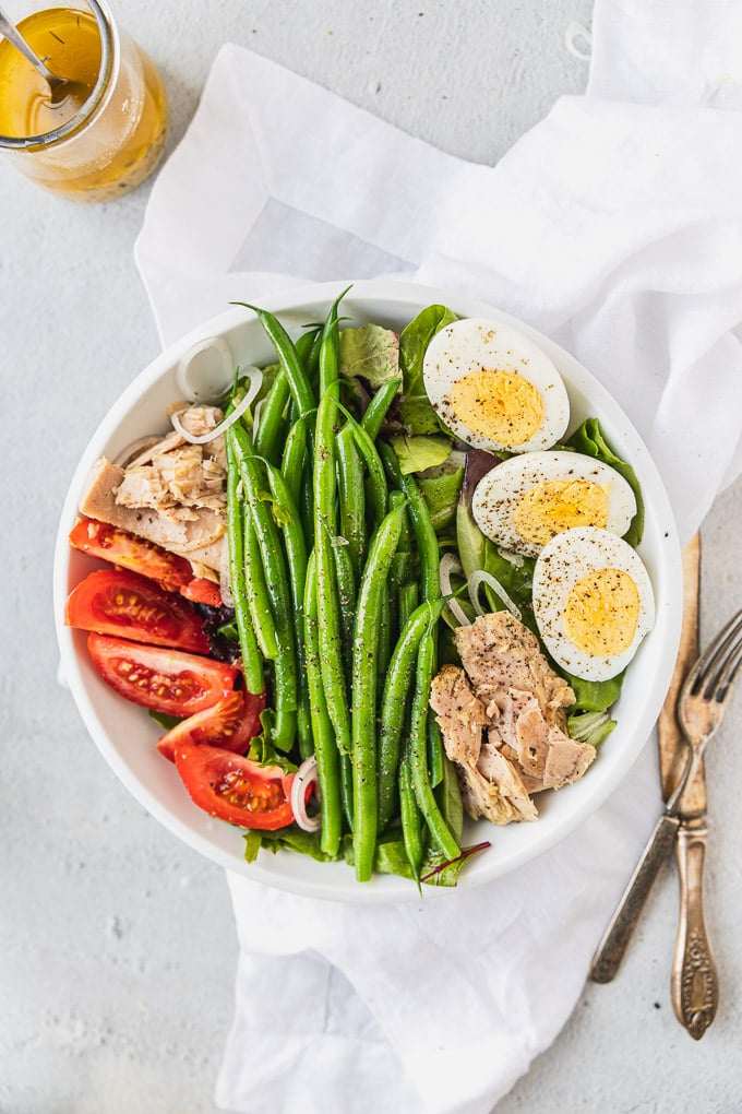 bowl with nicoise salad next to forks and knife and dressing