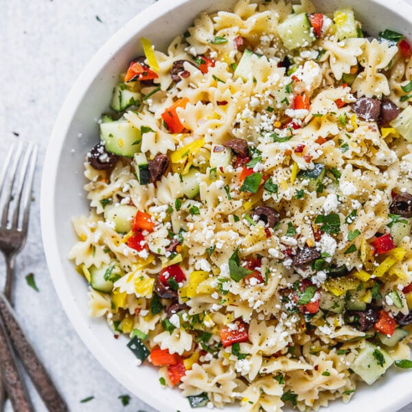 white bowl of bow tie pasta with mediterranean toppings