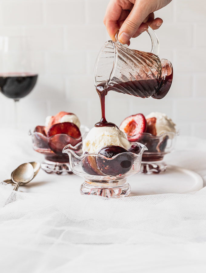 pouring wine sauce on ice cream with plums