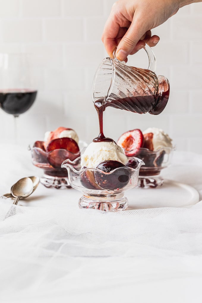 pouring wine sauce on ice cream with plums