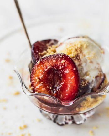 Sauteed plums in bowl with ice cream and spoon.