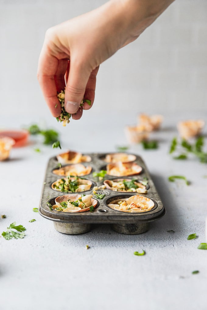 sprinkling cilantro on top of muffin tin with appetizer bites