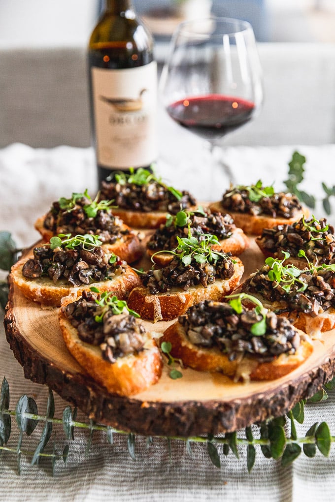 wooden serving plate with mushroom bruschetta next to wine