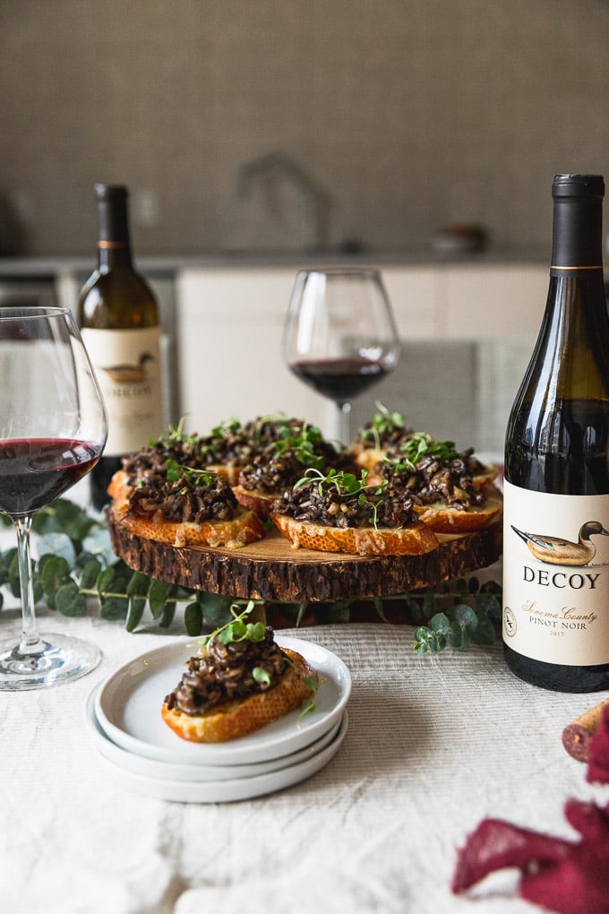 platter of mushroom bruschetta next to a bottle of wine and wine glasses