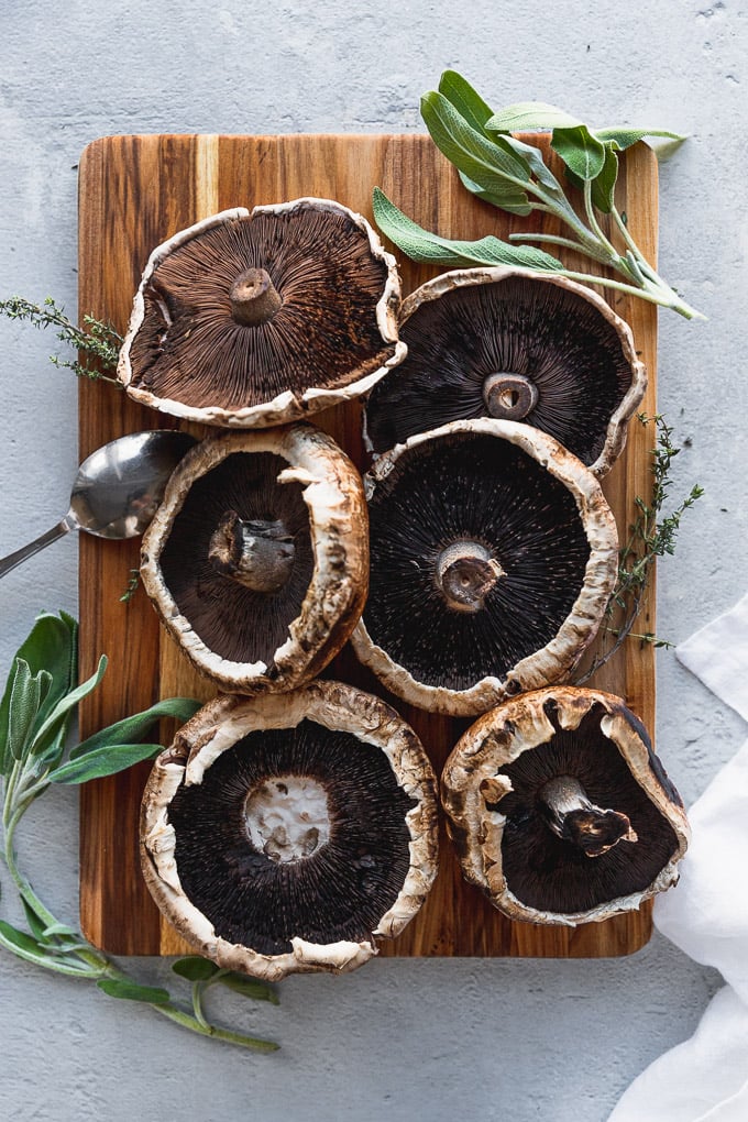 cutting board with portabella mushroom caps with fresh sage and thyme to make vegetarian stuffed portobello mushrooms