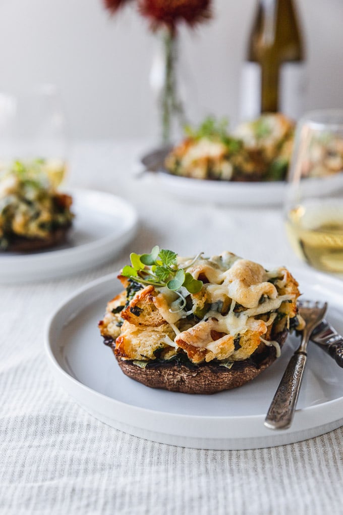 stuffed mushroom on a white plate with fork and knife on table next to wine with flowers in the background