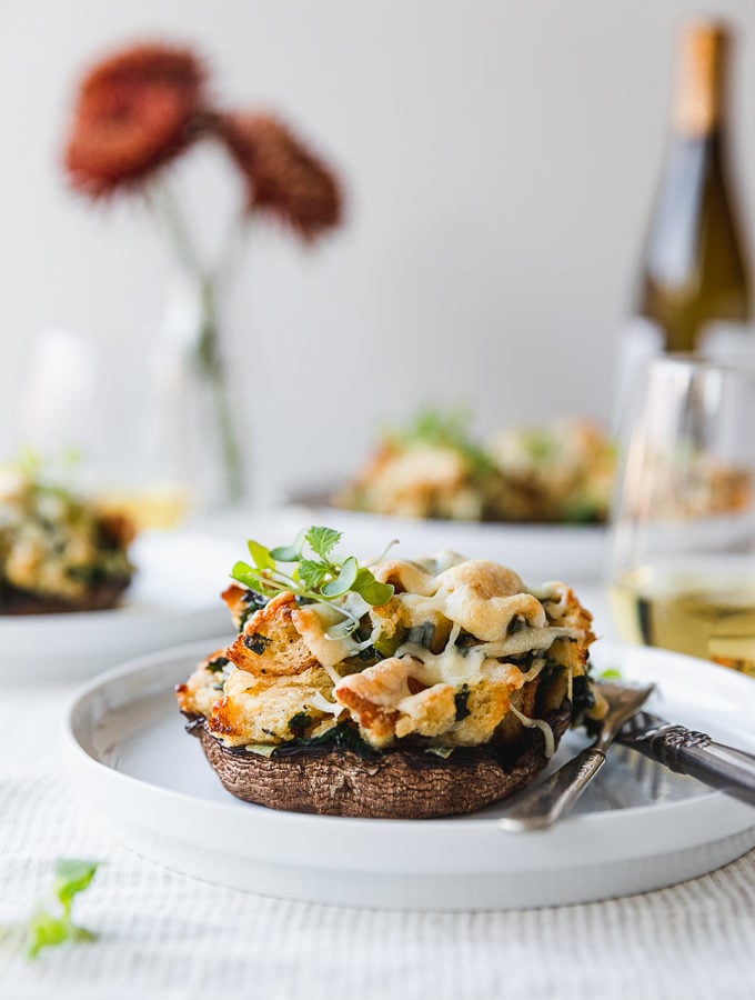 stuffed mushroom on a white plate with fork and knife on table next to wine