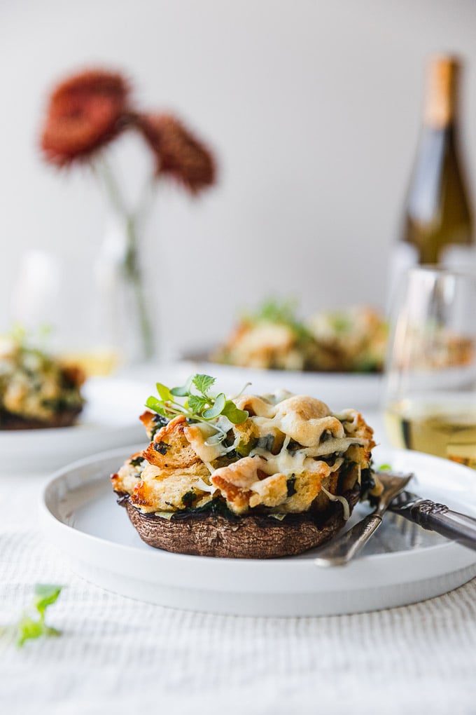 vegetarian stuffed mushroom on a white plate with fork and knife on table next to wine