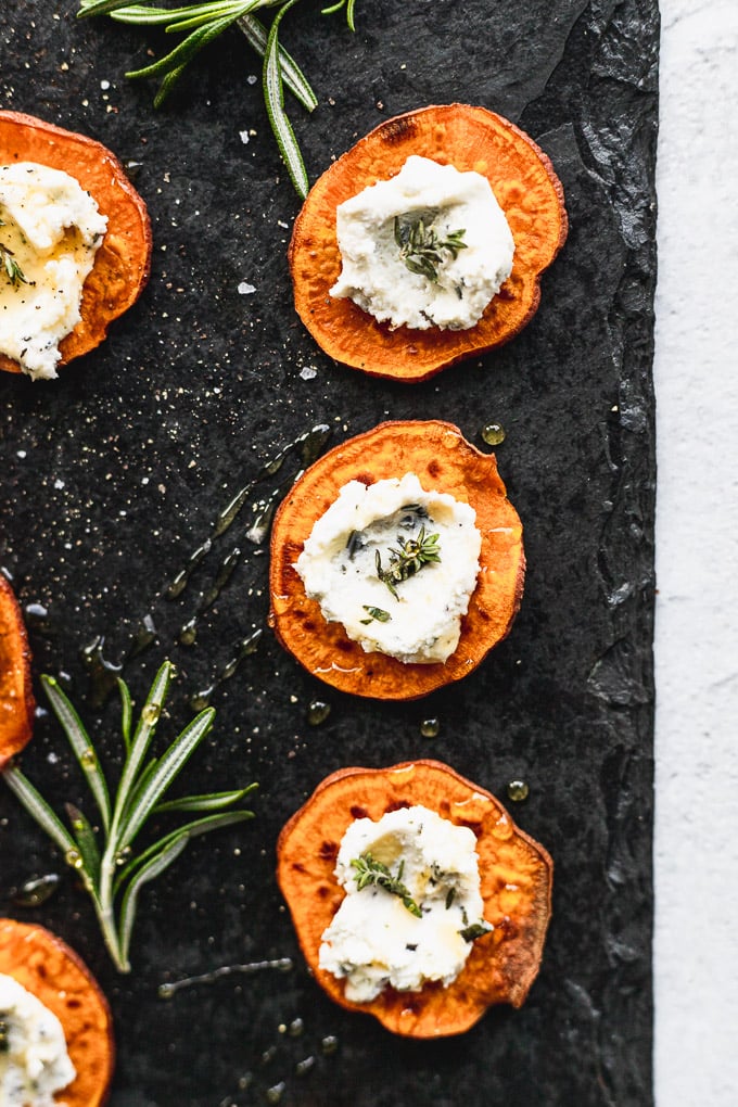 sweet potato goat cheese bites on black serving tray next to rosemary sprig