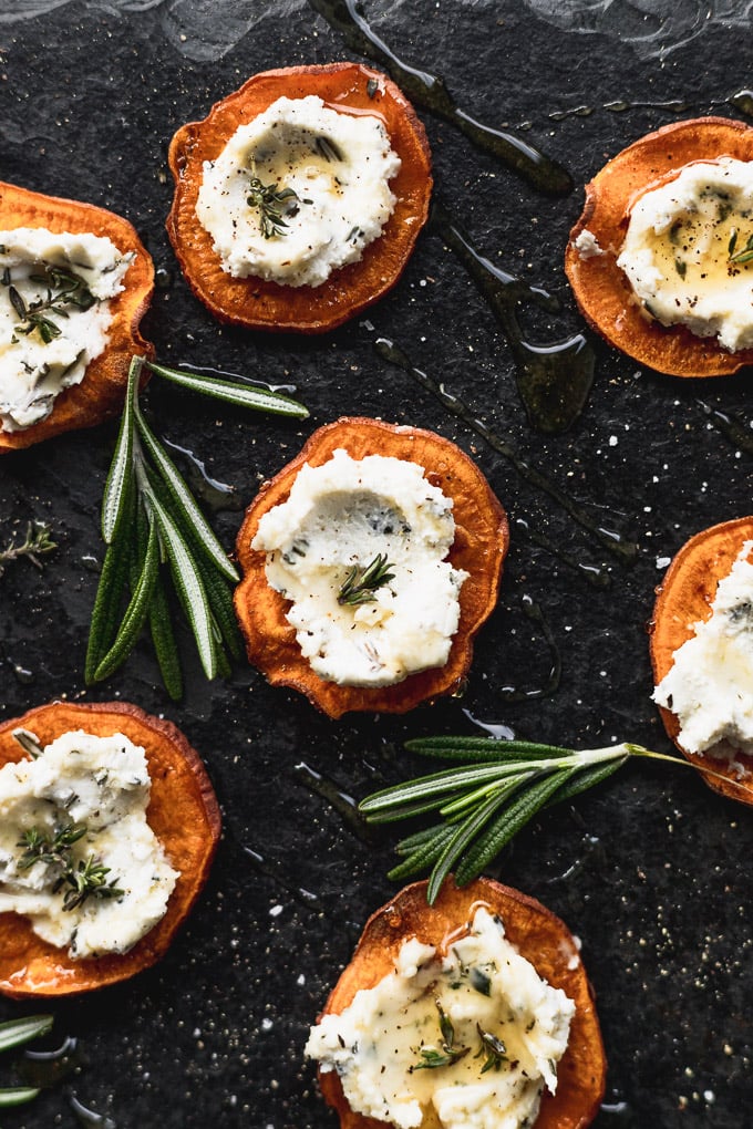 overhead sweet potato rounds on black serving tray next to rosemary sprigs