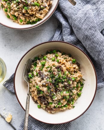 two bowls of mushroom risotto with forks next to blue striped linen and wine glass