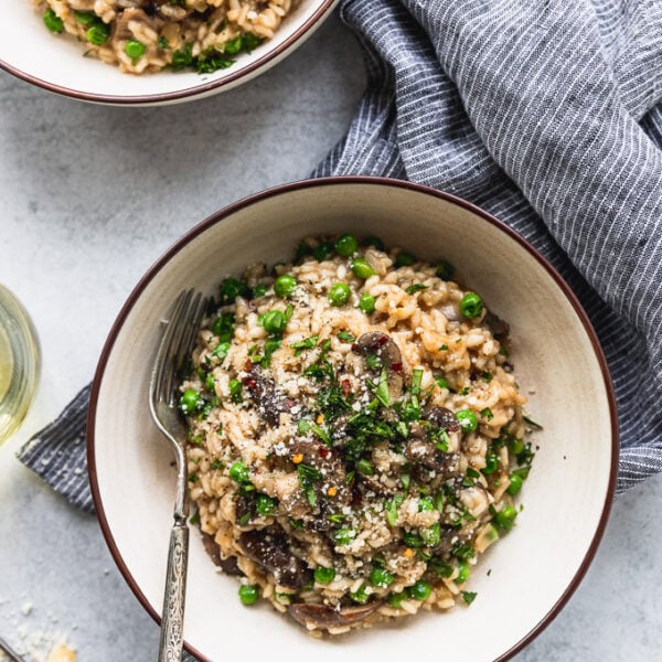 two bowls of mushroom risotto with forks next to blue striped linen and wine glass