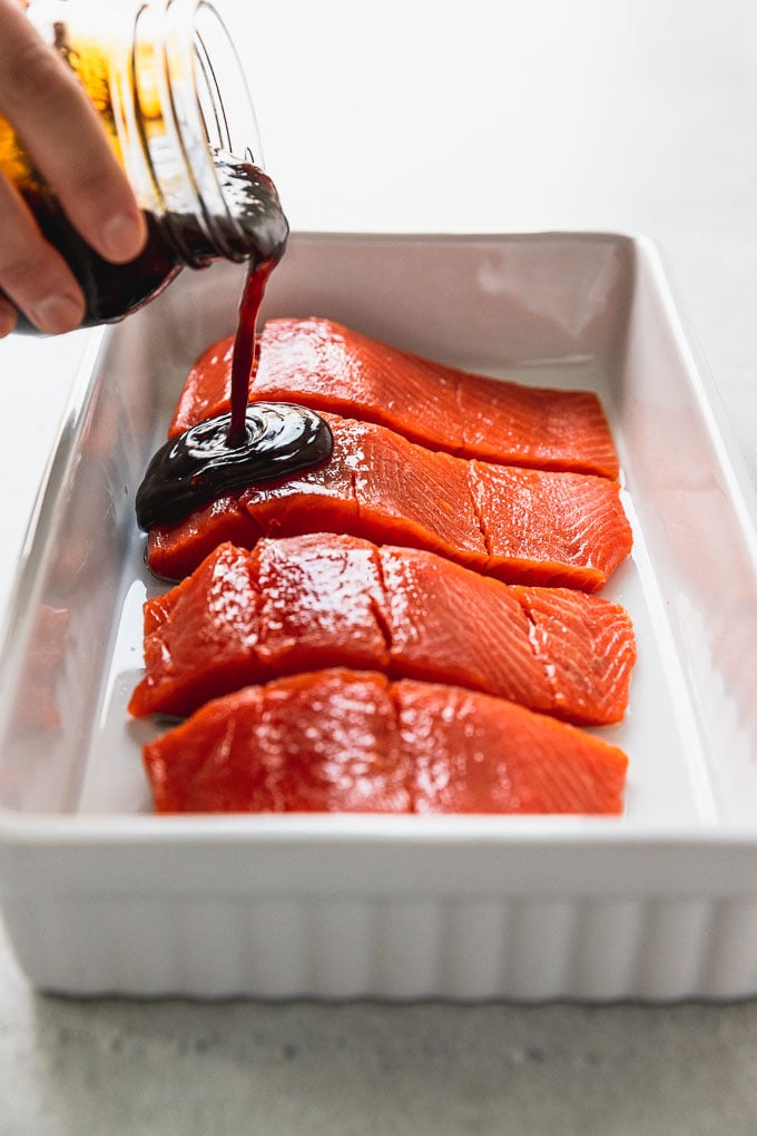 pouring teriyaki sauce on salmon filets in white baking dish