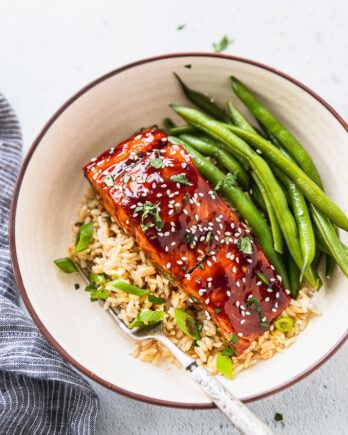 Bowl with rice, green onions, teriyaki salmon, and fresh green beans next to blue linen.