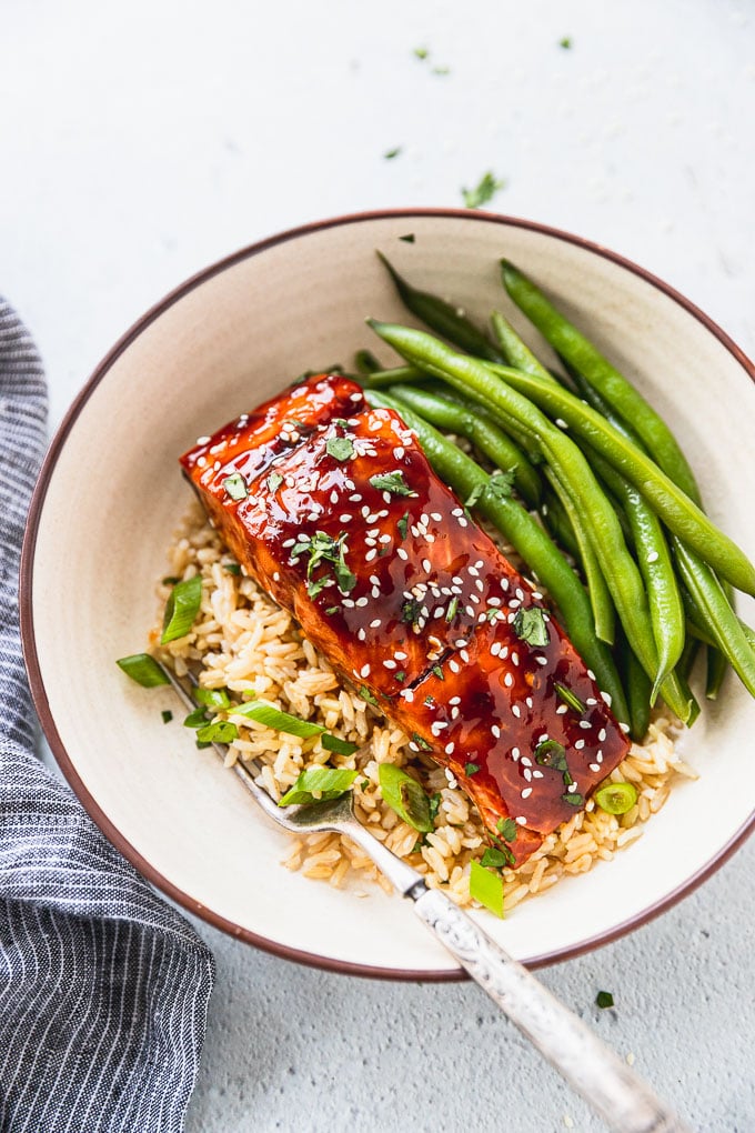 bowl with rice, green onions, teriyaki salmon, and fresh green beans next to blue linen