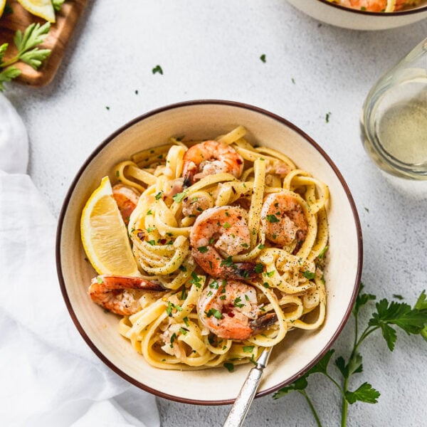 Two bowls of shrimp scampi next to board of lemon and parsley.