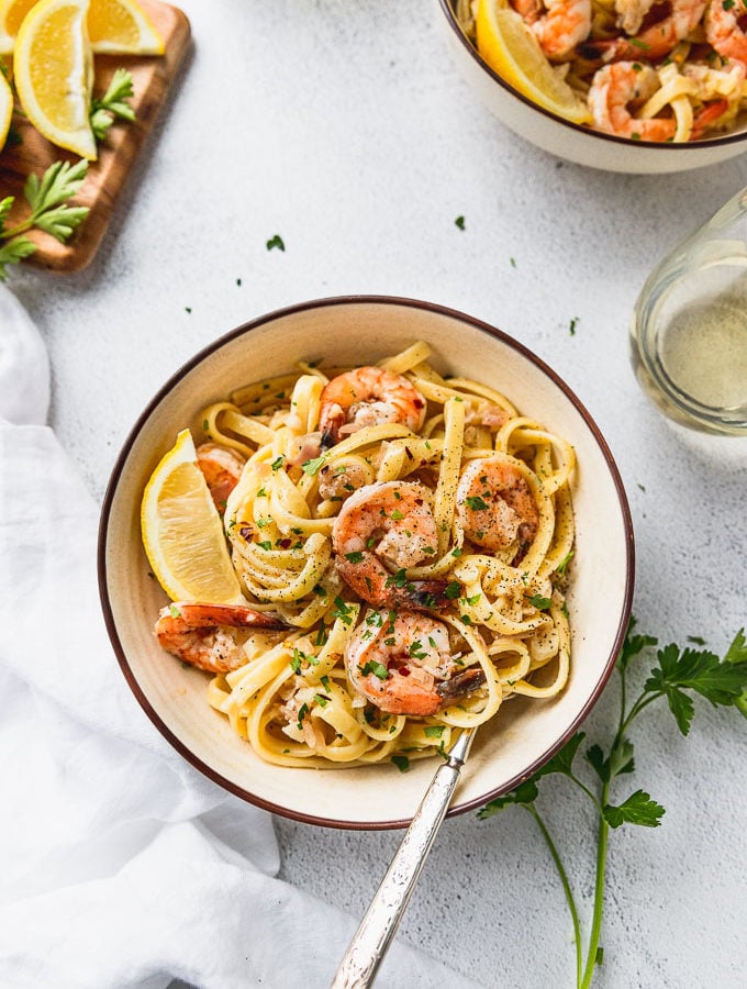 Two bowls of shrimp scampi next to board of lemon and parsley.