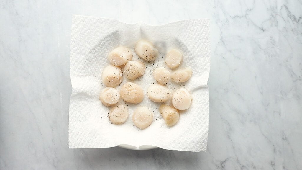 Scallops on paper towel with salt and pepper.