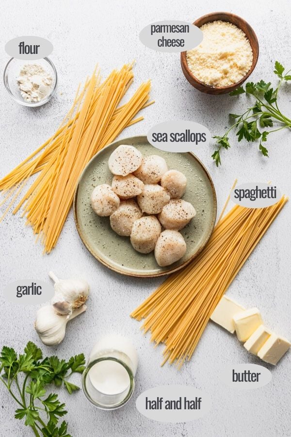 Plate of raw scallops next to spaghetti noodles, garlic, parsley, and parmesan with butter slices and flour - the pasta ingredients laid out.