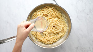 Pouring pasta water into sauce.