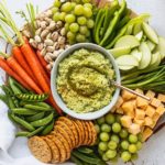 snack board with fresh vegetables and edamame hummus in the center with a spoon