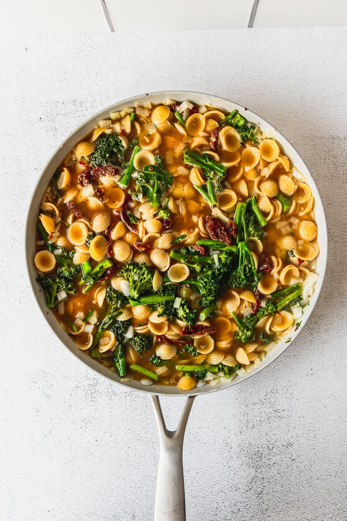 broccolini and sun dried tomatoes with dried orecchiette pasta and vegetable stock in skillet ready to cook