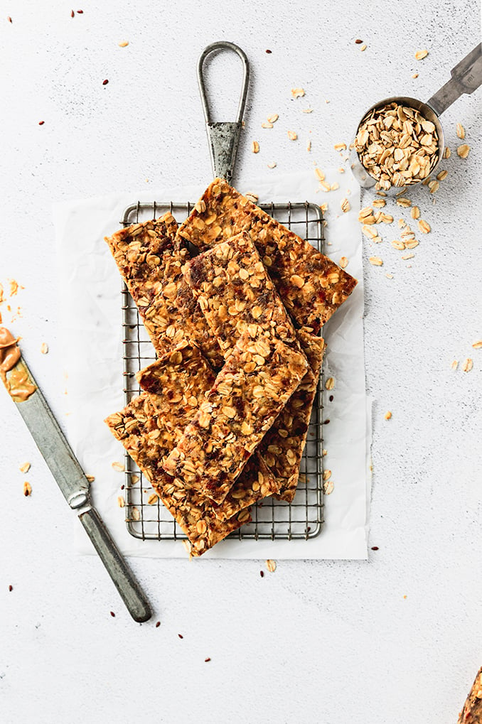 Pile of granola bars on cooling rack with knife and oats next to it.