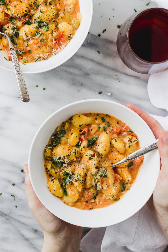 white bowl of vegetarian gnocchi with spinach and tomatoes
