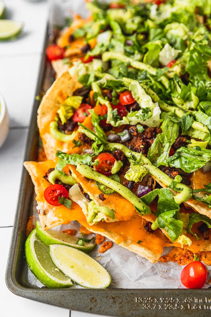 up close view of nachos on sheet pan with avocado sauce, tomatoes, and lettuce