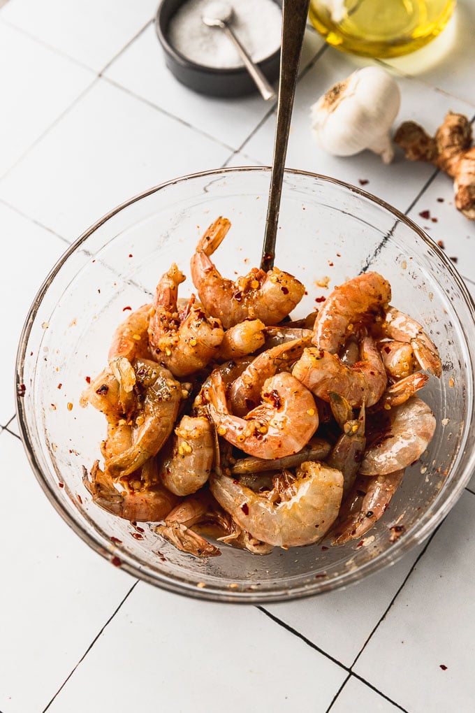 glass bowl with raw shell-on shrimp in marinade with spoon