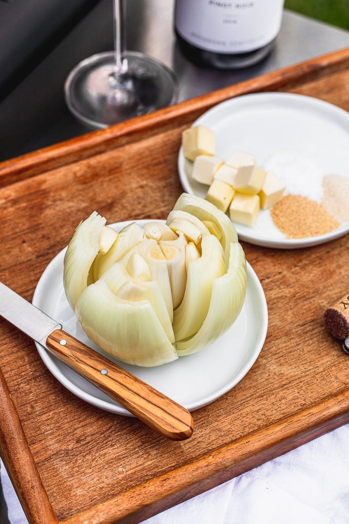 two white plates on a wooden serving tray. one plate has a whole onion with garlic in the layers and a knife next to it. the other plate has cubed butter, onion, and garlic powder.