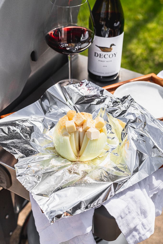 whole onion with butter and garlic on top on a piece of foil with a wine glass and bottle in the background