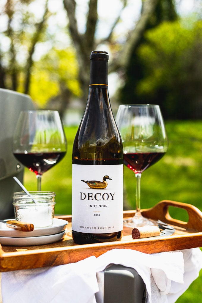 bottle of Decoy wine on a wooden serving tray next to two glasses of red wine, white plates, and a mini bowl of salt with a spoon