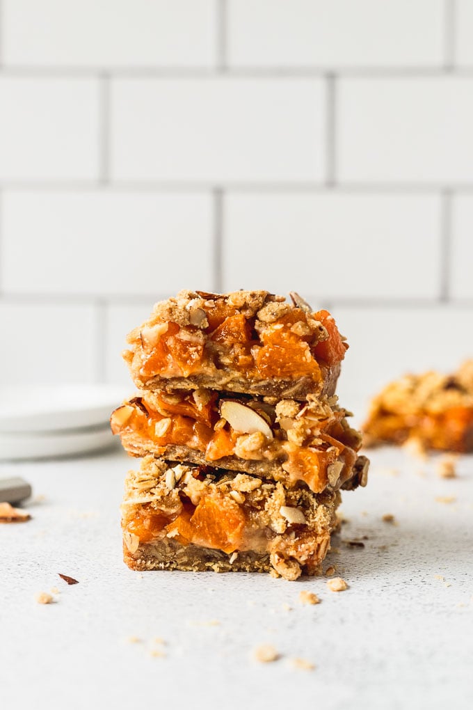 three almond crumble bars stacked on each other with white subway tile in background