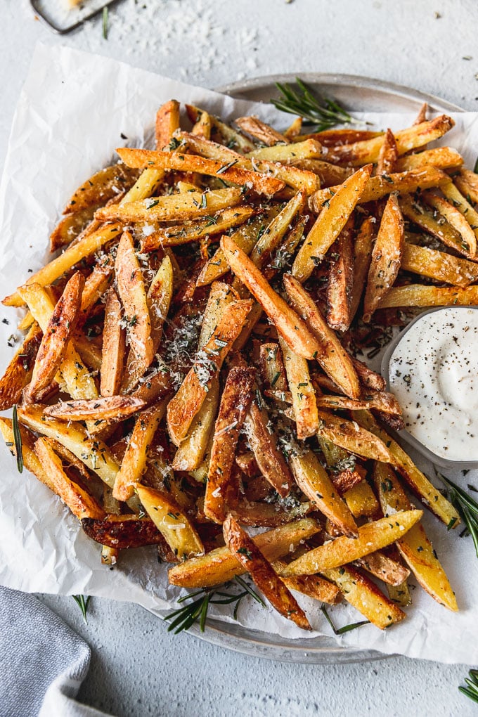 Crispy Baked Rosemary Garlic Parmesan Fries on a tray with parchment paper next to a small bowl of dipping sauce
