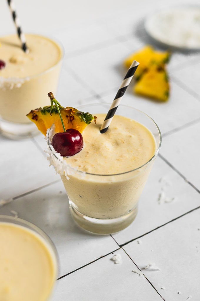 pina colada milkshake garnished with cherry, pineapple wedge and straw and a cocktail behind it