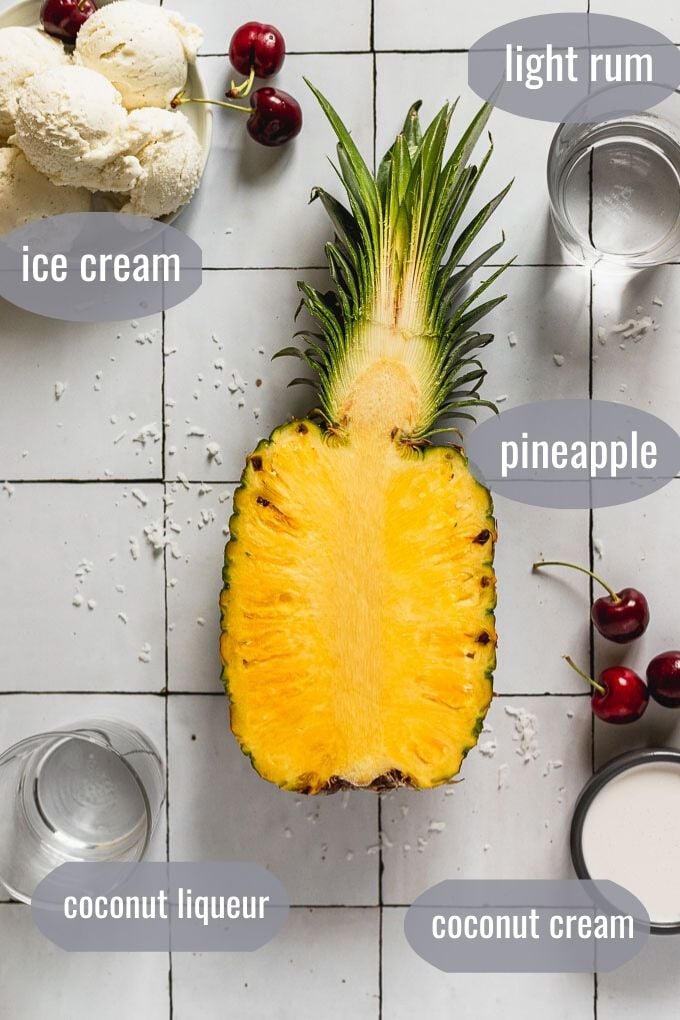 flat lay with pineapple sliced open, ice cream, liquor, cherries, and coconut cream