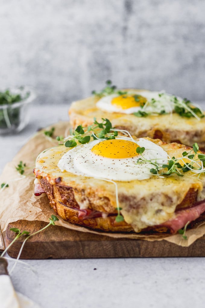 Two croque madame sandwiches on wooden board with microgreens.