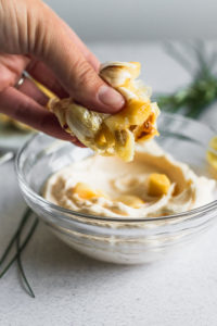 hand squeezing garlic cloves into bowl of mayonnaise