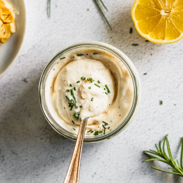 jar of garlic aioli with spoon swired in it next to rosemary