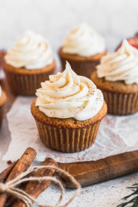 apple cider cupcake with cream cheese frosting on parchment paper and wood tray