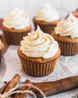 apple cider cupcake with cream cheese frosting on parchment paper and wood tray