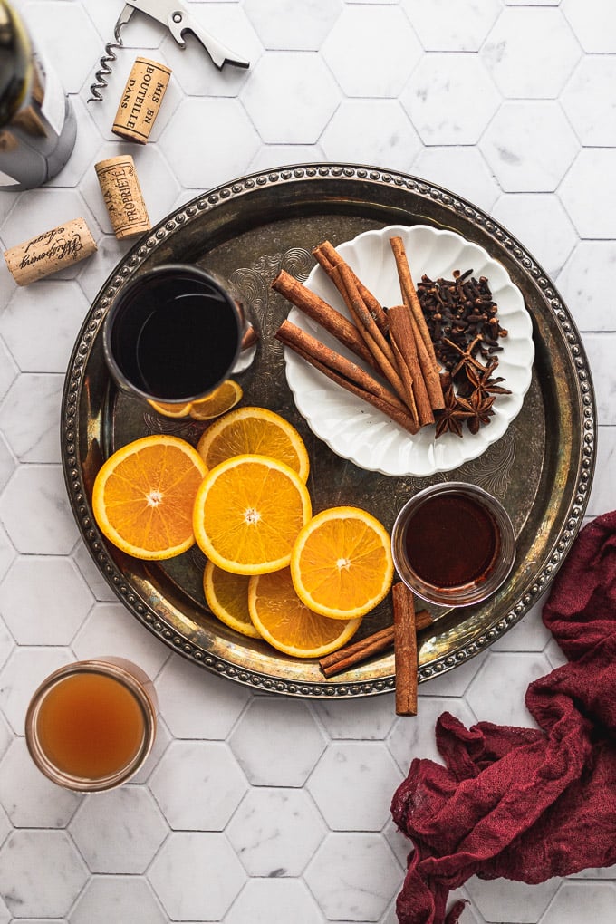 Tray with cinnamon sticks, cloves, star anise, oranges, wine, and cider.