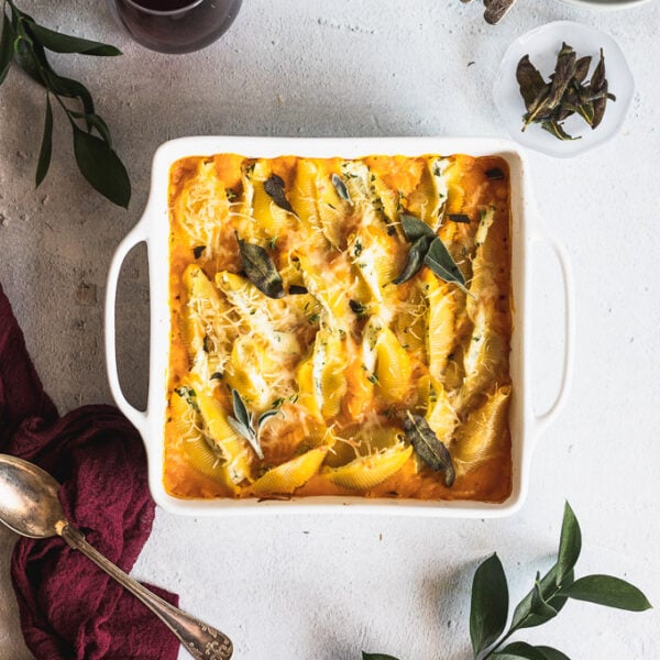 white baking dish with stuffed shells next to a spoon and greenery