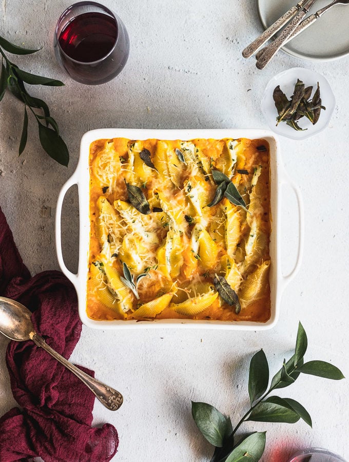 white baking dish with stuffed shells next to a spoon and greenery