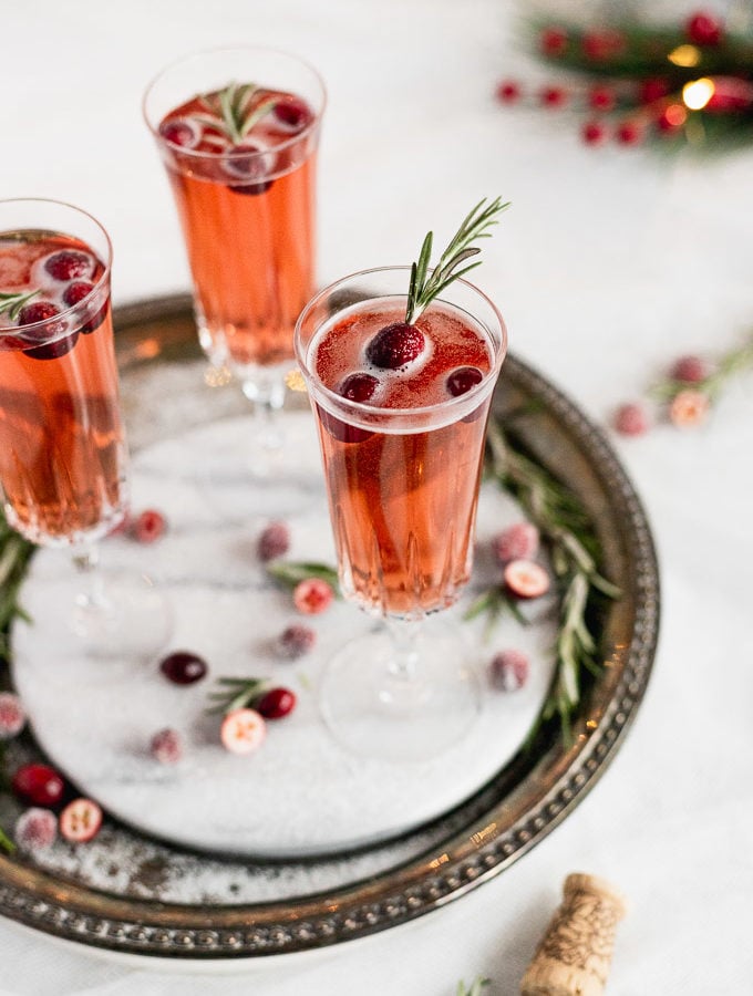 three glasses of cranberry rosemary prosecco on marble tray with sugar coated cranberries around