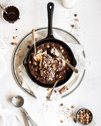 overhead brownie skillet with three spoons and ice cream with chocolate drizzle