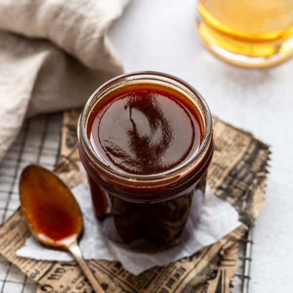 jar of bourbon bbq sauce with spoon and bourbon glass next to it
